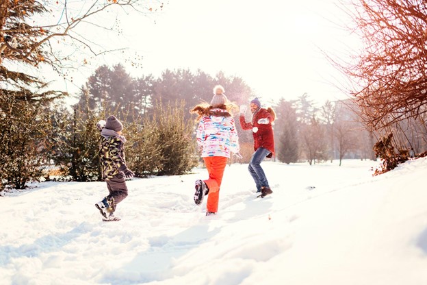 Family having fun outdoors in winter time. Father with son and daughter making snowballs and having a snowball fight.