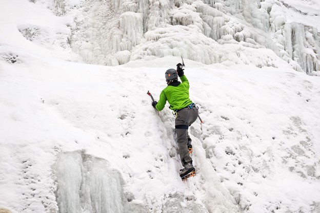 climber with ice axes climbing up on a frozen waterfall 