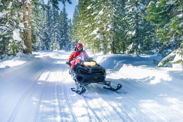 Mother and son driving a snowmobile through a path in the woods