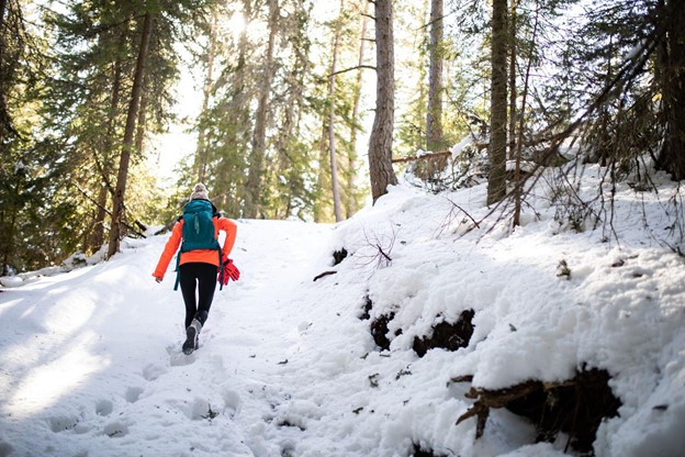 A young woman in hiking equipment hiking up a snowy slope in the woods